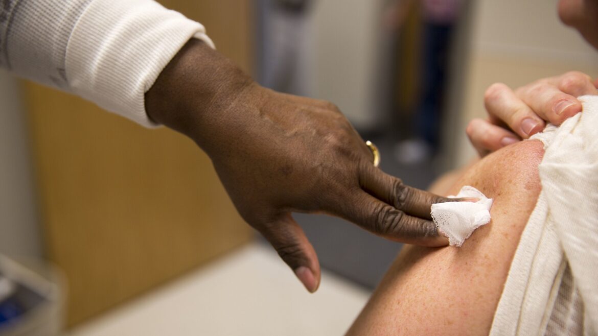 Health care worker presses gauze on a patient's arm after a flu shot as flu season 2026 starts early